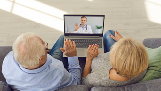 overhead view of an older couple sitting on a couch and talking to their doctor on a laptop