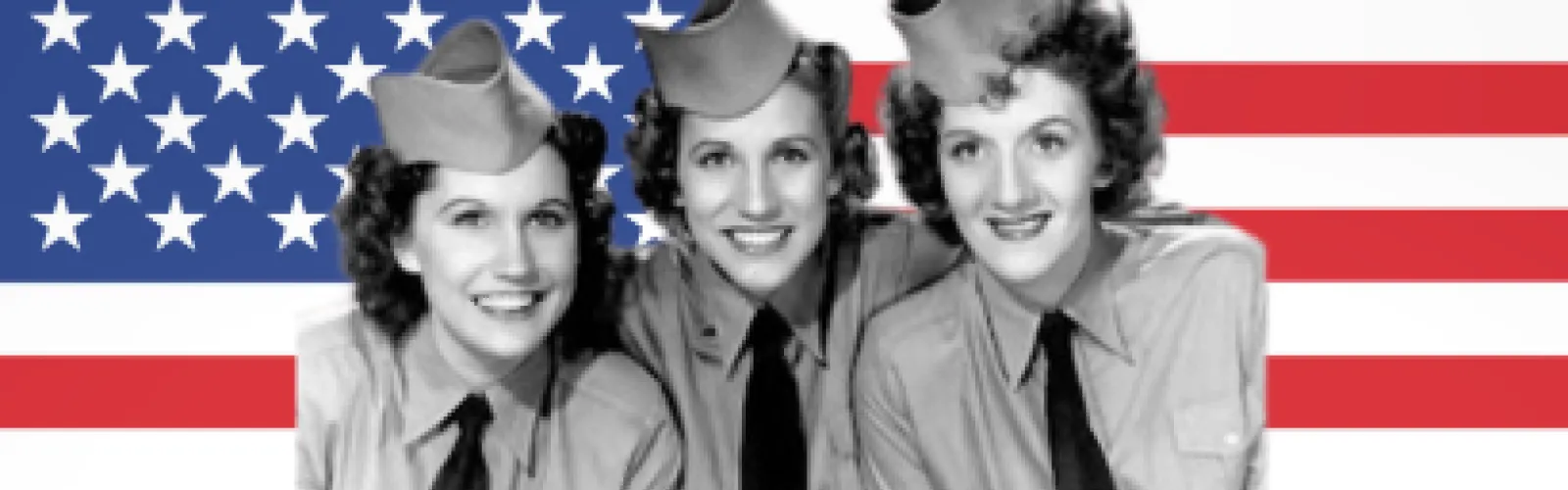 Three women in military uniforms posing and smiling in front of an American flag backdrop.
