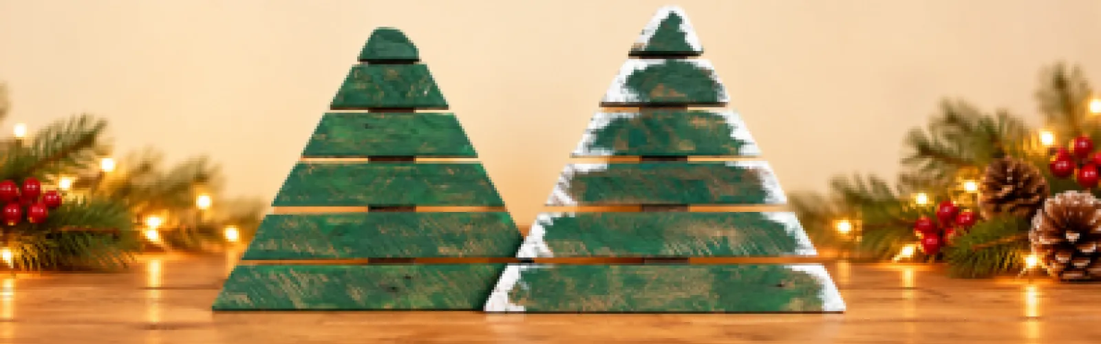Two rustic green wooden Christmas tree on a warm-lit table, framed by pine branches and glowing festive lights.